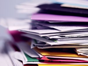 Image shoes a stack of documents and reports, some in colourful folders